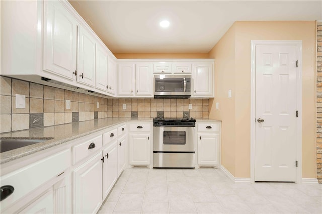 kitchen with light tile patterned floors, light stone counters, backsplash, stainless steel appliances, and white cabinets