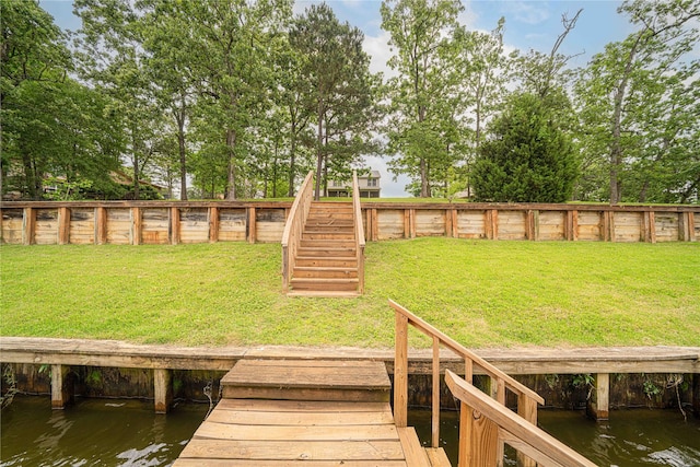 view of dock with a water view, a fenced backyard, a lawn, and stairway