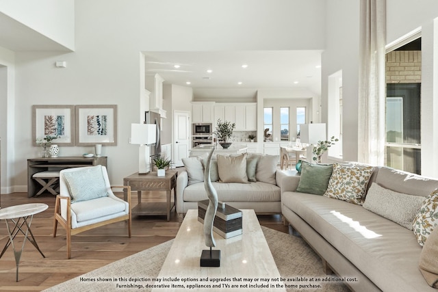 living room featuring baseboards, light wood-style flooring, recessed lighting, and a towering ceiling