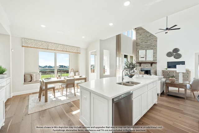 kitchen with a sink, light wood-type flooring, open floor plan, stainless steel dishwasher, and a stone fireplace