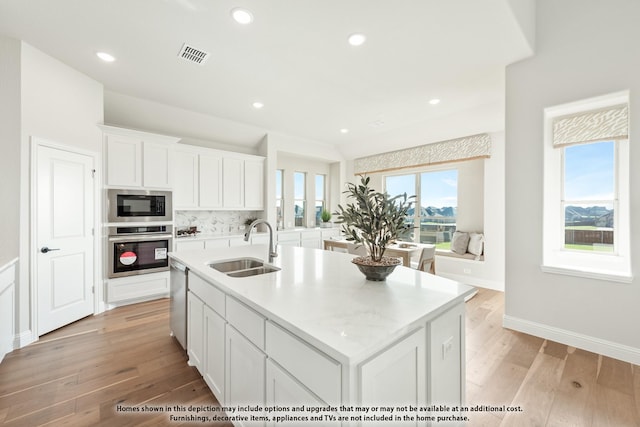 kitchen featuring appliances with stainless steel finishes, visible vents, a sink, white cabinetry, and light wood-type flooring