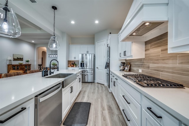 kitchen featuring white cabinetry, decorative backsplash, arched walkways, custom range hood, and appliances with stainless steel finishes