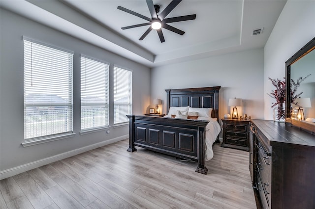 bedroom featuring light wood-type flooring, baseboards, a tray ceiling, and visible vents