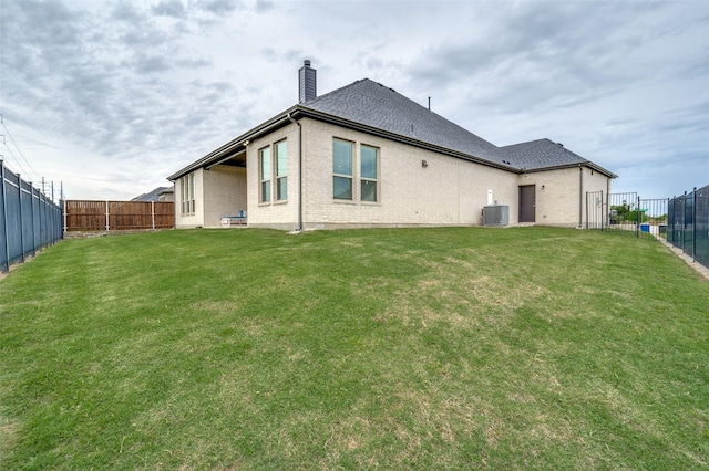 rear view of house with a fenced backyard, a lawn, a chimney, and central AC