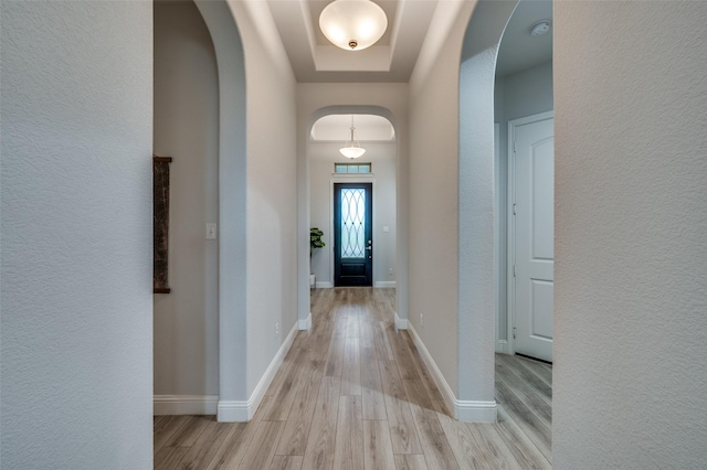 foyer entrance featuring light wood finished floors, a raised ceiling, arched walkways, and a textured wall