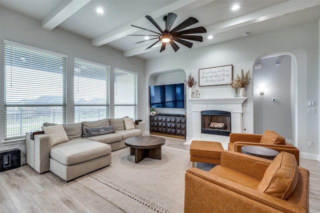 living room with beam ceiling, light wood-type flooring, a wealth of natural light, arched walkways, and a ceiling fan