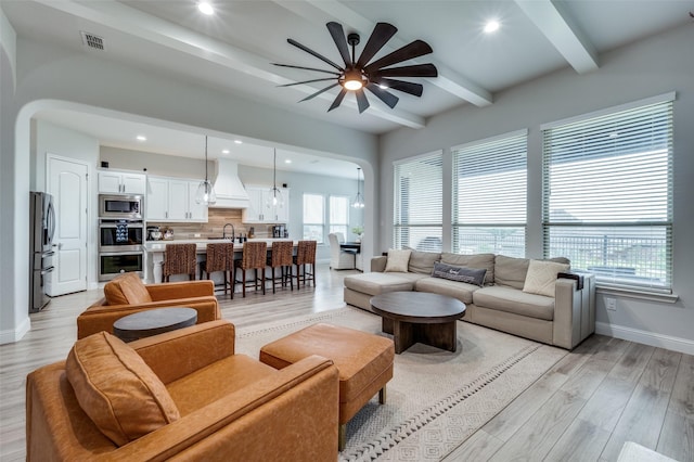 living room with a ceiling fan, light wood-style flooring, baseboards, visible vents, and beamed ceiling