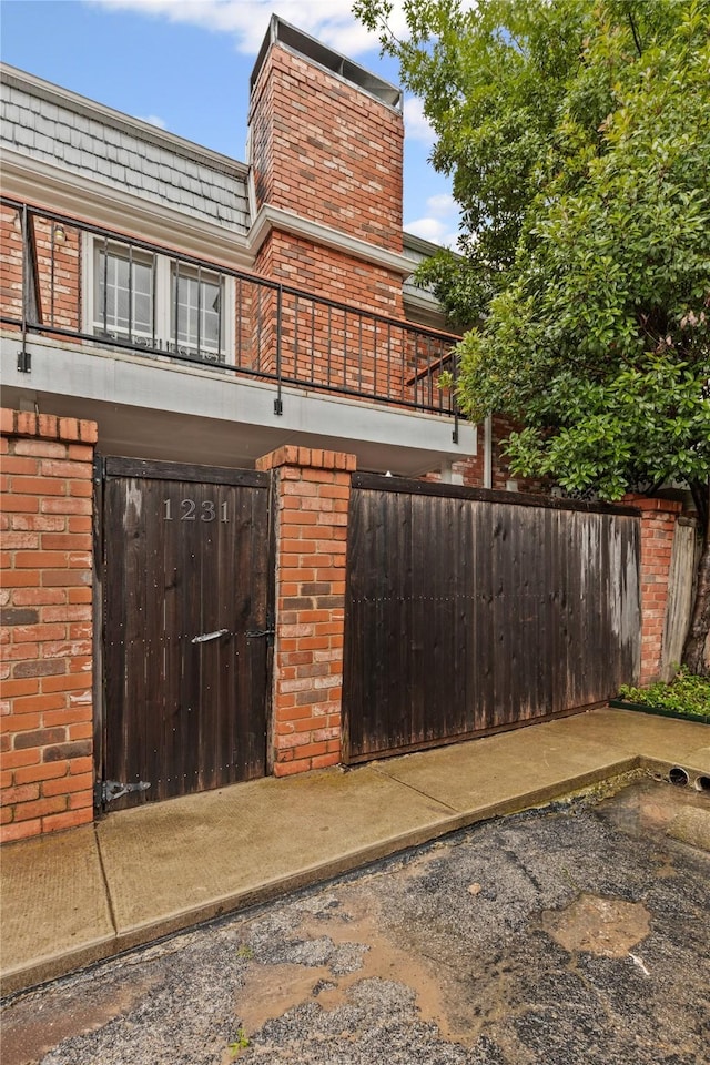 view of side of home with a balcony, brick siding, fence private yard, and a gate