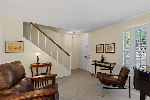 sitting room featuring stairway, light colored carpet, and baseboards