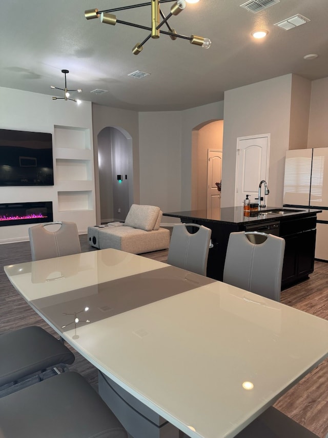 kitchen featuring arched walkways, open floor plan, an island with sink, and wood finished floors