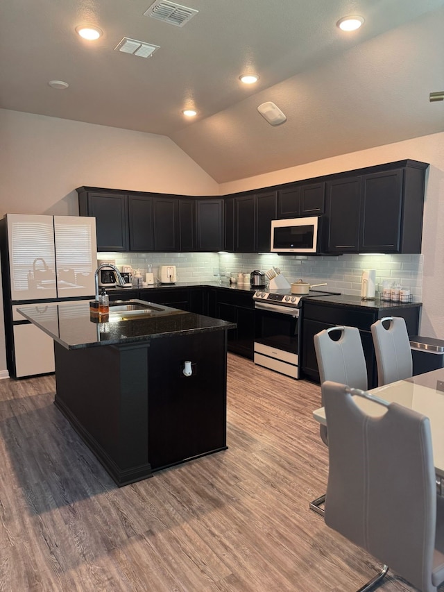 kitchen featuring lofted ceiling, dark cabinets, stainless steel electric range, a sink, and white microwave