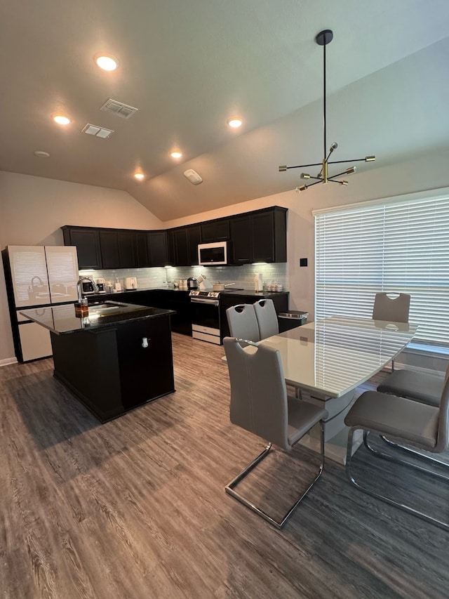 kitchen with white appliances, dark cabinets, dark countertops, and wood finished floors