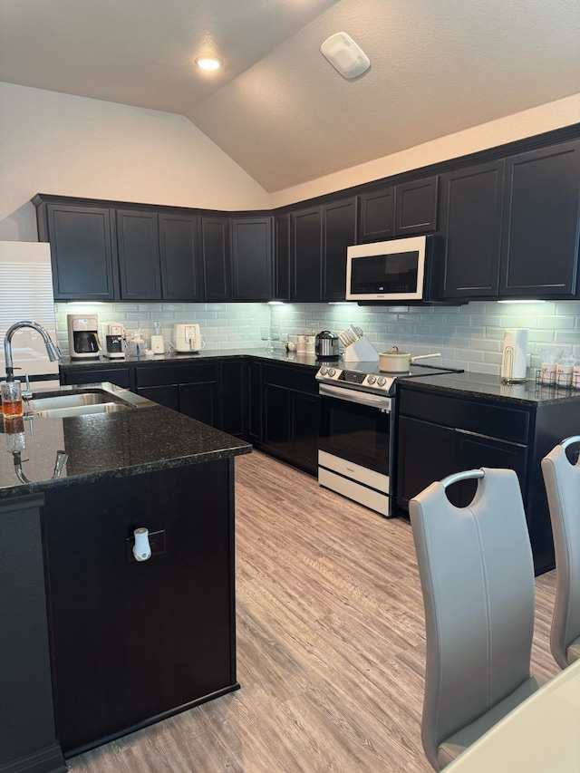 kitchen featuring a sink, dark stone countertops, white microwave, vaulted ceiling, and electric stove