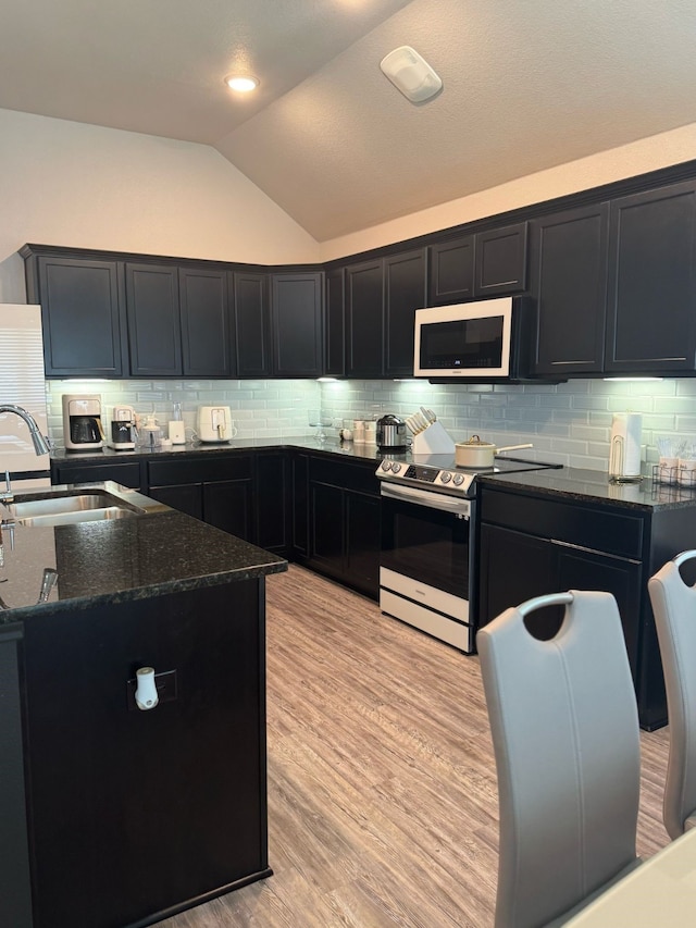 kitchen with lofted ceiling, a sink, white microwave, dark stone counters, and range with electric stovetop
