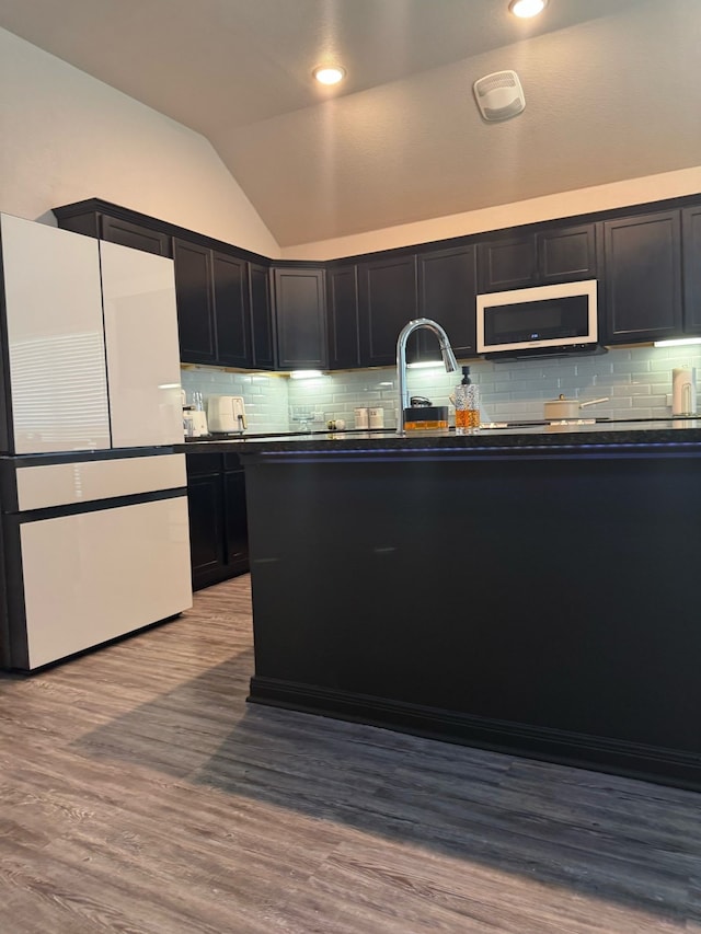 kitchen featuring lofted ceiling, white appliances, dark cabinets, dark countertops, and tasteful backsplash