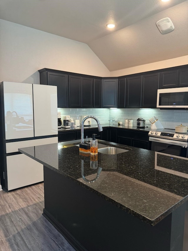 kitchen featuring dark stone countertops, a sink, white appliances, vaulted ceiling, and dark cabinetry