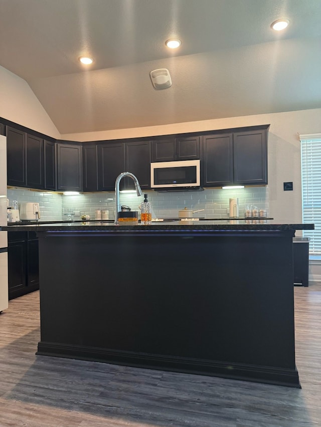 kitchen with dark countertops, white microwave, tasteful backsplash, and vaulted ceiling