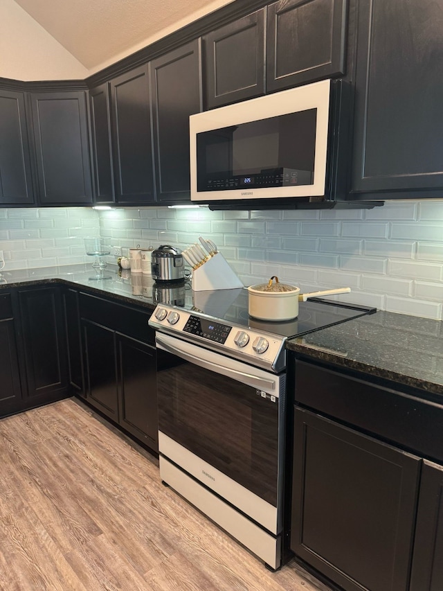 kitchen with dark cabinets, tasteful backsplash, dark stone countertops, and electric stove