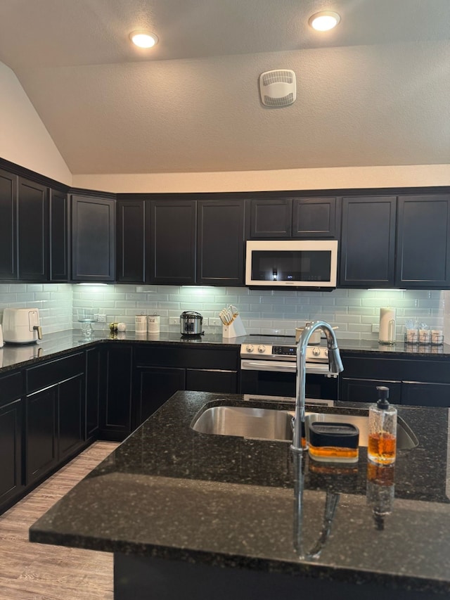 kitchen featuring backsplash, light wood-style floors, dark cabinets, and dark stone countertops