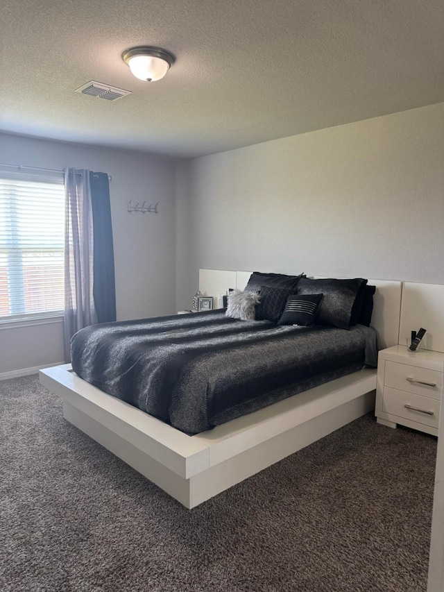 bedroom featuring dark carpet, visible vents, and a textured ceiling
