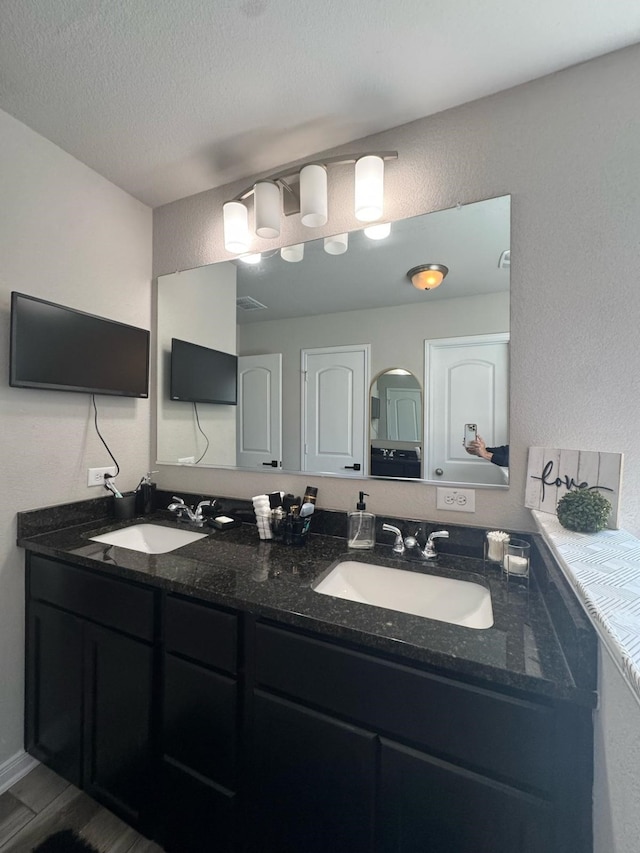 full bath with double vanity, a textured wall, and a sink