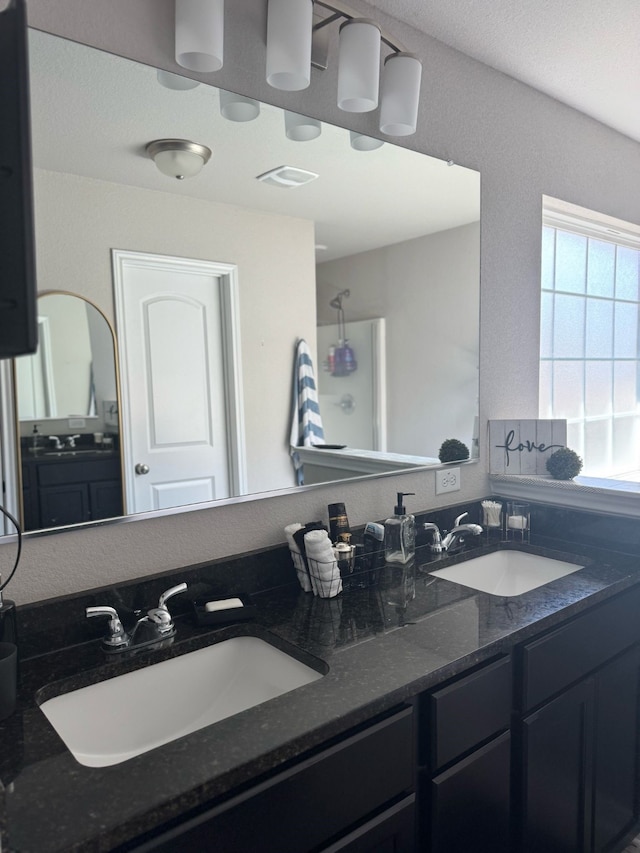 bathroom with a shower, visible vents, double vanity, and a sink