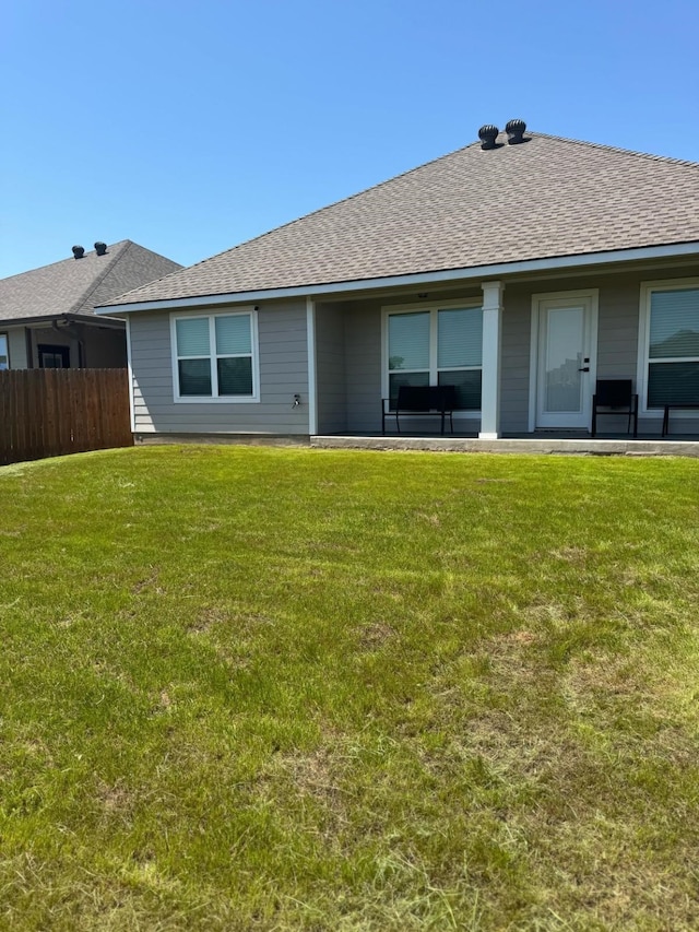 rear view of house featuring a lawn, roof with shingles, and fence