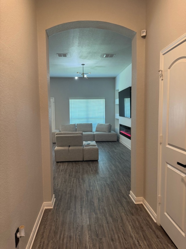 hallway featuring arched walkways, baseboards, visible vents, and dark wood finished floors