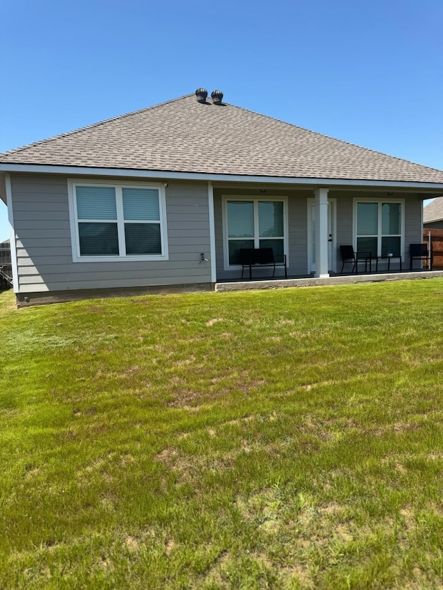 rear view of house with a shingled roof and a lawn