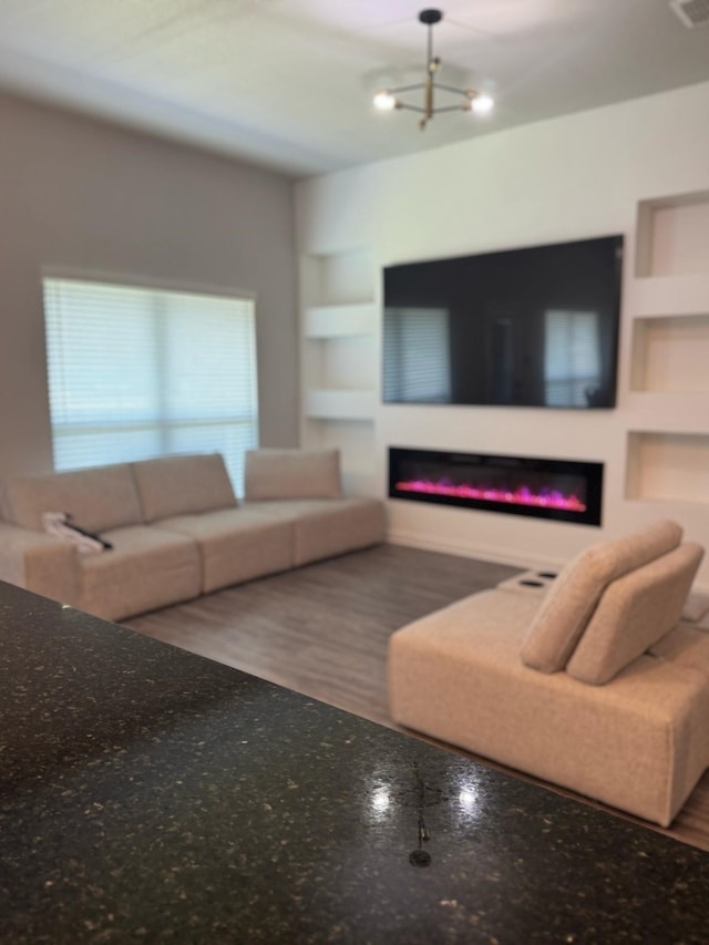 living room featuring a glass covered fireplace, a chandelier, and built in shelves