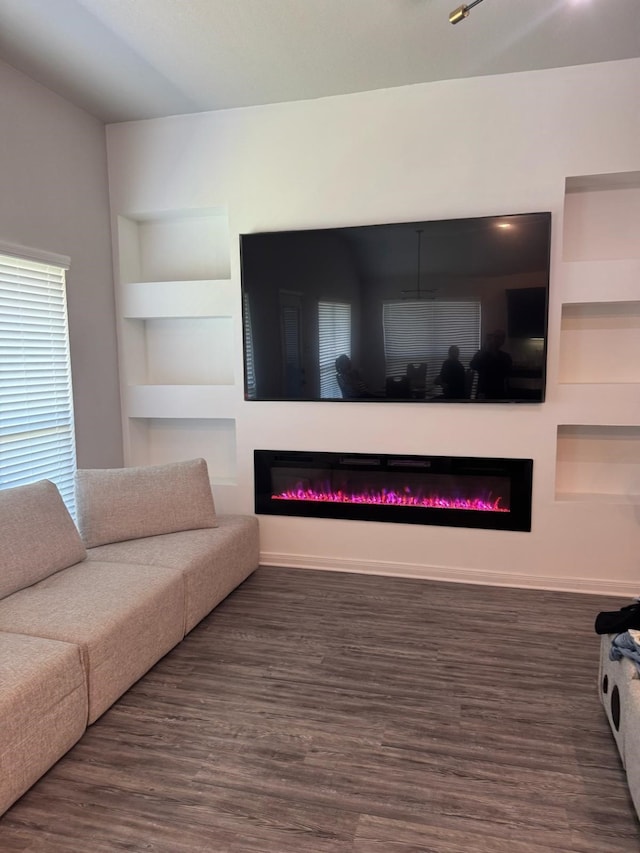 living area with wood finished floors, baseboards, a glass covered fireplace, and built in features