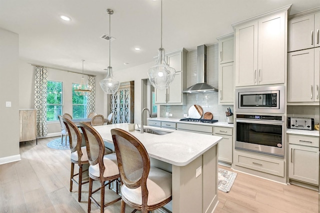 1504 Bearpath Way, Gunter, TX 75058 - kitchen with stainless steel appliances, wall chimney range hood, tasteful backsplash, an island with sink, and light wood-style flooring