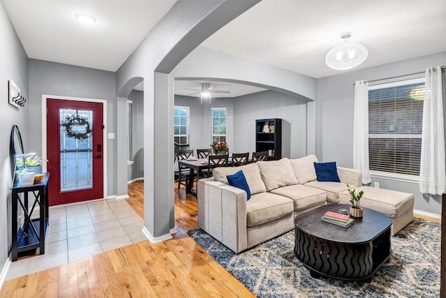 living room featuring wood finished floors, baseboards, arched walkways, and ceiling fan with notable chandelier