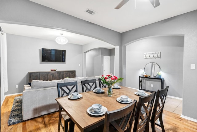 dining room with visible vents, ceiling fan, light wood finished floors, arched walkways, and baseboards