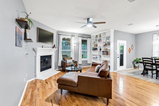 living room with baseboards, a glass covered fireplace, visible vents, ceiling fan, and wood finished floors