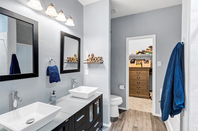 full bathroom with toilet, a walk in closet, a sink, and wood finished floors