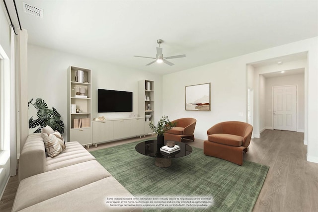 living area featuring wood finished floors, a ceiling fan, visible vents, baseboards, and built in shelves