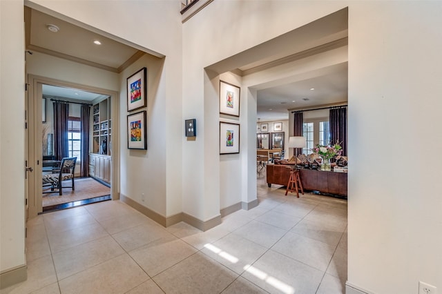 corridor featuring light tile patterned floors, ornamental molding, and baseboards