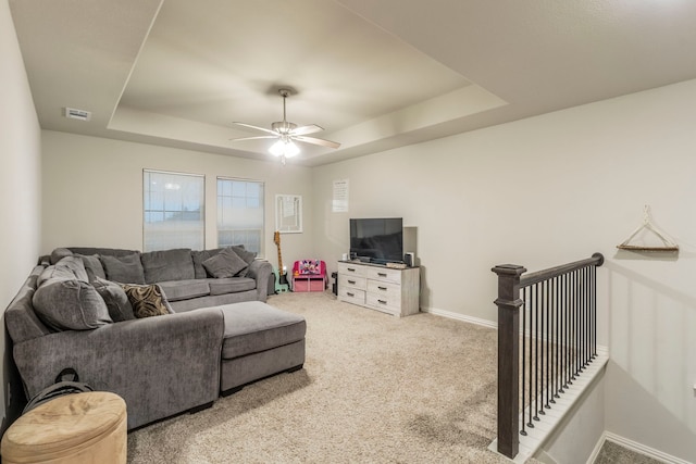 carpeted living room featuring ceiling fan, a raised ceiling, baseboards, and visible vents