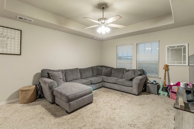 carpeted living room with a ceiling fan, a raised ceiling, baseboards, and visible vents