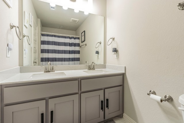bathroom featuring toilet, visible vents, double vanity, and a sink
