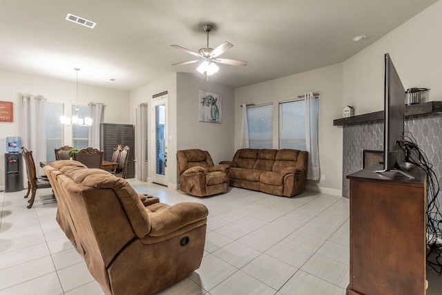 living room featuring light tile patterned floors, ceiling fan with notable chandelier, a fireplace, visible vents, and baseboards