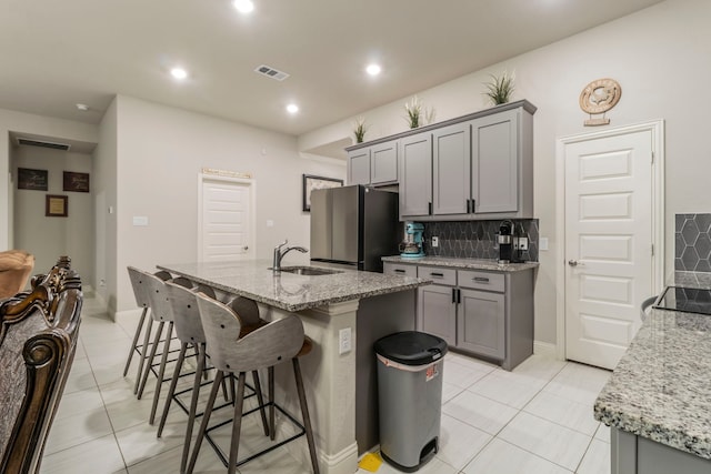 kitchen with freestanding refrigerator, gray cabinetry, visible vents, and a sink