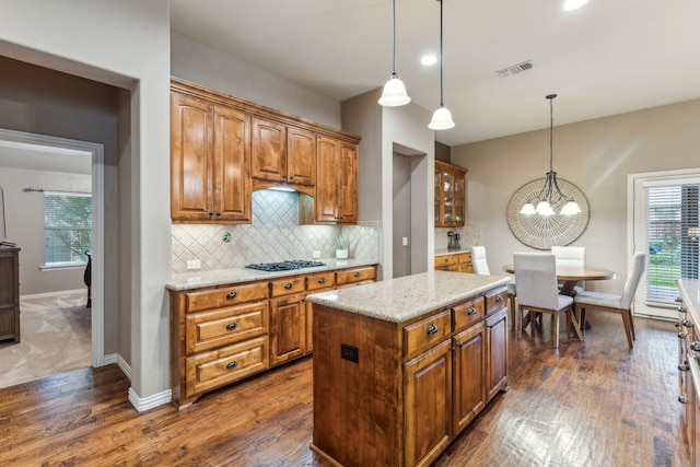 kitchen featuring brown cabinetry, dark wood-style flooring, light stone countertops, gas cooktop, and a chandelier
