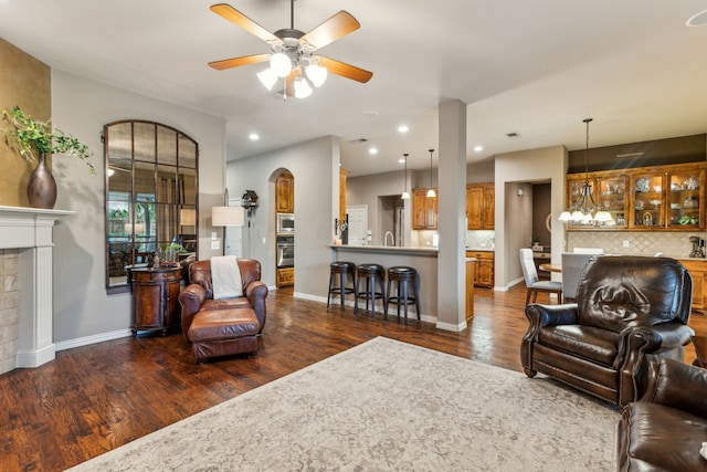 living area with baseboards, ceiling fan, arched walkways, a fireplace, and dark wood-style floors