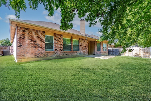 back of house with fence, a patio area, brick siding, a yard, and a chimney