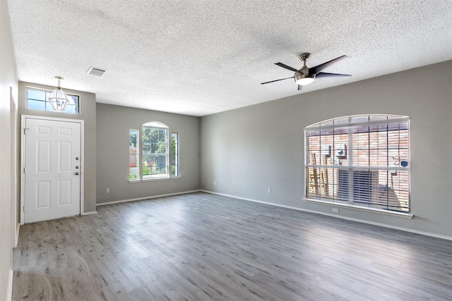 interior space featuring ceiling fan with notable chandelier, wood finished floors, a textured ceiling, visible vents, and baseboards