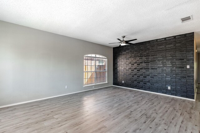 spare room with wood finished floors, a textured ceiling, visible vents, ceiling fan, and baseboards