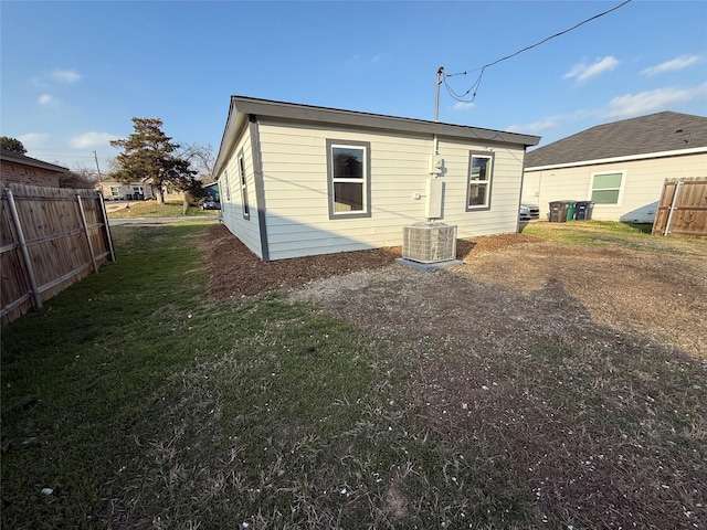 rear view of property featuring a yard, central AC unit, and fence