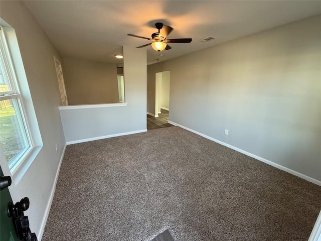 spare room featuring baseboards, a ceiling fan, visible vents, and dark carpet
